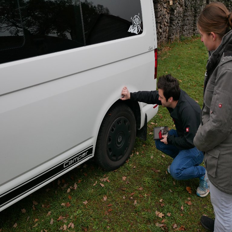 Fahrzeug Gutachter Sebastian Wöllenweber erfasst einen Streifschaden am Radlauf eines weißen VW Bullis
