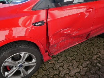 Roter Ford Kuga nach einem Verkehrsunfall mit sichtbaren Beschädigungen an der linken Tür