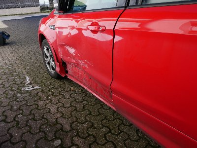 Zerkratzte linke Autotür und beschädigter Seitenspiegel eines roten Ford Kuga nach einem Parkunfall