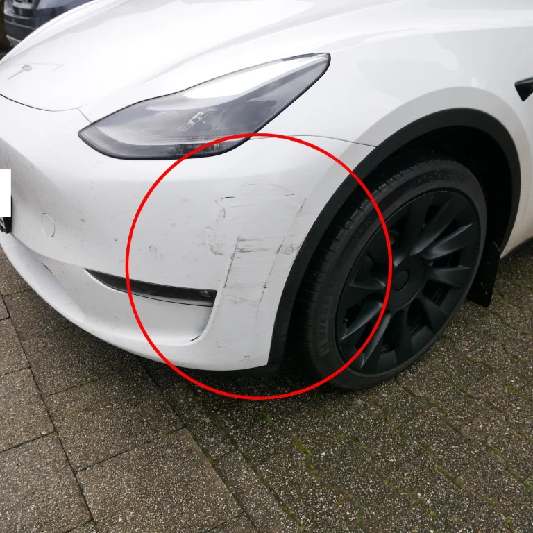 Nahaufnahme von Schäden am linken Scheinwerfer und der Front eines weißen Tesla Model S nach einem Zusammenstoß