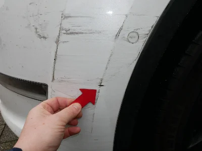 Weißer Tesla Model S mit sichtbaren Unfallschäden vorne links, inklusive zerkratzter Stoßstange