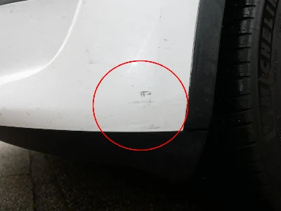 Schäden durch einen Zusammenstoß an der vorderen linken Seite eines weißen Tesla Model S, fokussiert auf Stoßstange und Kotflügel
