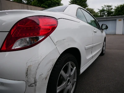 Detailansicht von Lackabplatzungen und Dellen am hinteren rechten Kotflügel eines weißen Peugeot 307 Cabrio